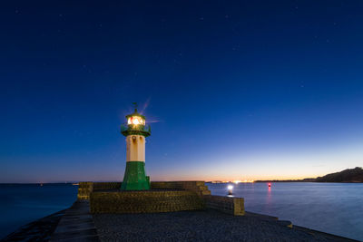 Lighthouse by sea against sky at night