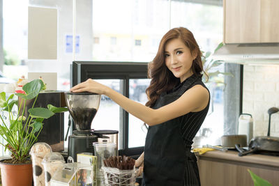 Portrait of young woman making drink in blender at cafe