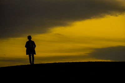 Rear view of man walking on road against sky during sunset