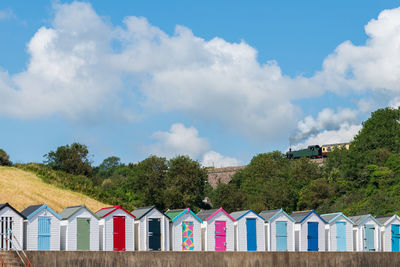Colourful beach houses. row of  beach huts with steam train on stone viaduct against blue sky.