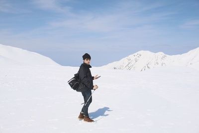 Portrait of male hiker in sunglasses standing on snow against sky