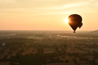 Hot air balloon flying over landscape against sky during sunset