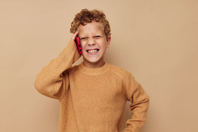 Cute boy talking on phone against beige background