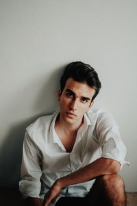 Portrait of young man sitting against wall at home