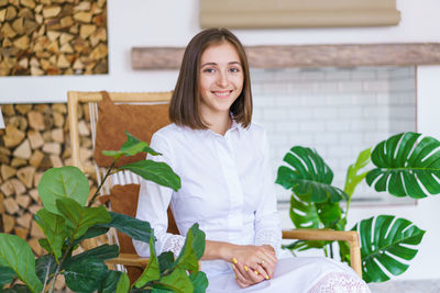 Successful young woman is sitting in chair and smiling and looking at camera.