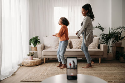 Happy mother and daughter dancing and recording video through smart phone at home