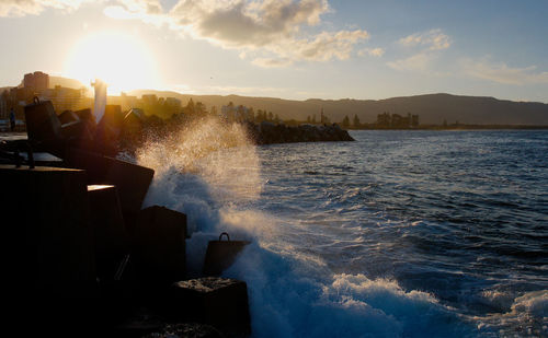 Water splashing in sea against sky during sunset