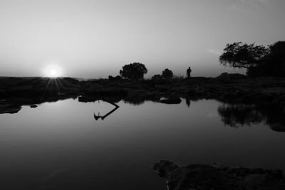Silhouette trees by lake against sky