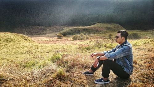 Side view of young man sitting on land