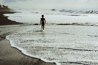 Rear view of boy walking at seashore