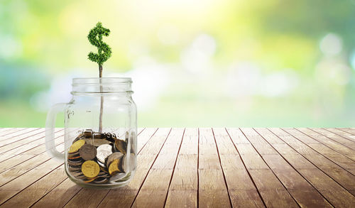 Close-up of dollar symbol and coins in mason jar on wooden table