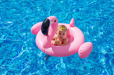 Cute girl sitting on pool raft in swimming pool