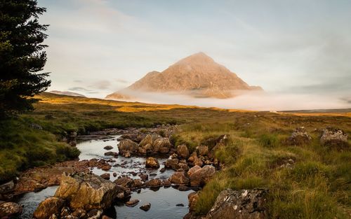 Rocks on stream by field against buachaille etive mor in foggy weather