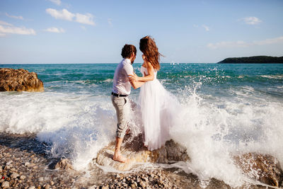 Young couple standing at beach against sky