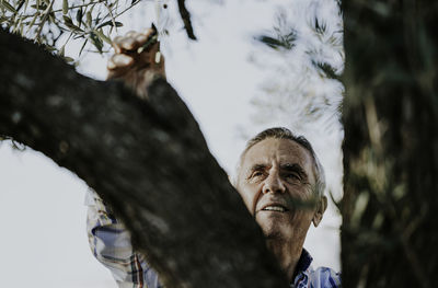 Low angle view of thoughtful man by tree against sky