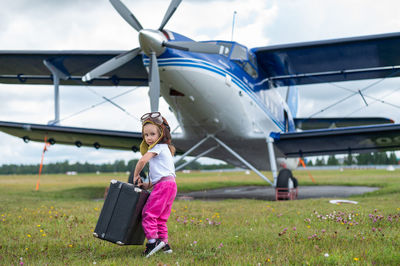 Full length of girl with suitcase against air plane