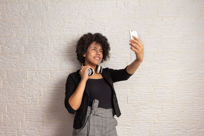 Young woman using phone while standing against wall