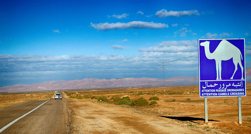 Road sign on land against blue sky