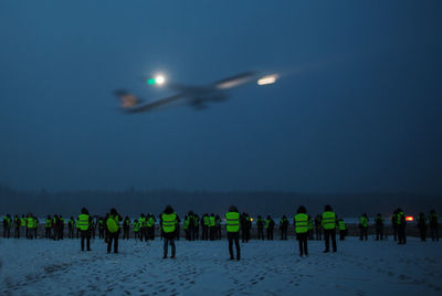 People standing on snow covered field against sky at night