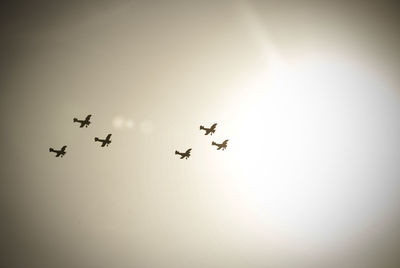 Low angle view of silhouette biplanes flying against sky