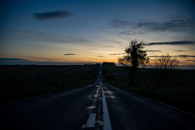 Empty road along landscape at sunset