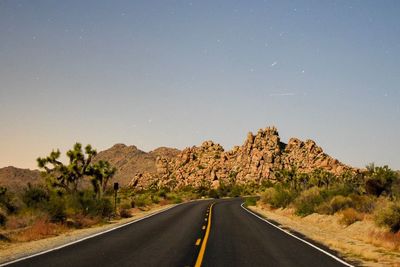 Empty road leading towards rock formations against clear sky