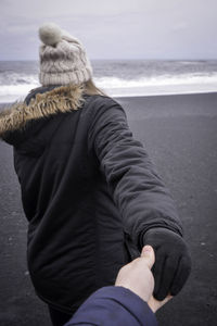 Close-up of people with holding hands at beach against sky