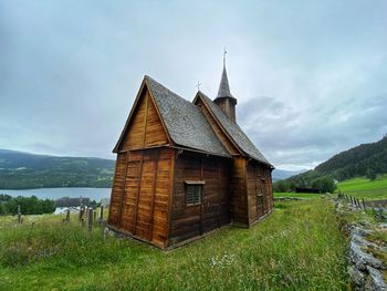 Built structure on field by lake against sky. lomen stave church