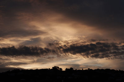 Low angle view of silhouette trees against dramatic sky