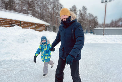Young caucasian bearded man skating with his son, holding hands.