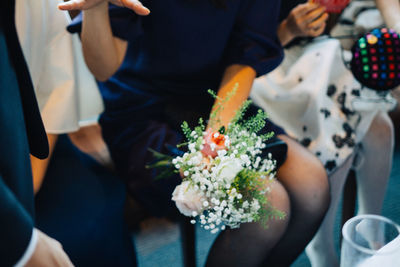 Midsection of man holding bouquet in front of roses