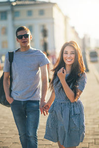 Portrait of smiling young woman walking with man on sidewalk