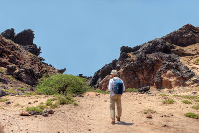 Rear view of man walking against rock formations and sky