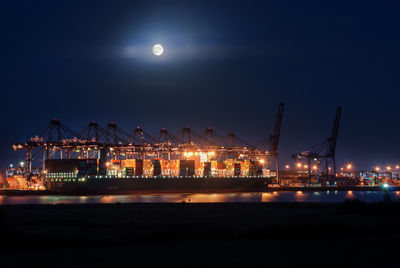 Illuminated pier by sea against sky at night