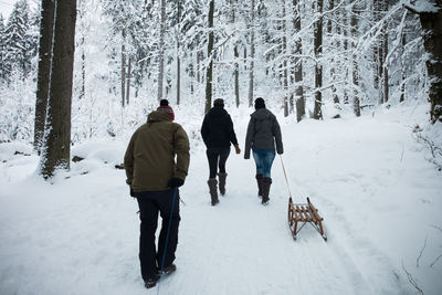 Rear view of people wearing warm clothing walking on snow covered land in forest