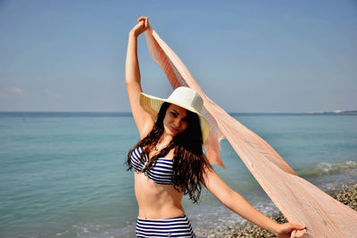 Portrait of beautiful woman holding scarf while standing against sea at beach