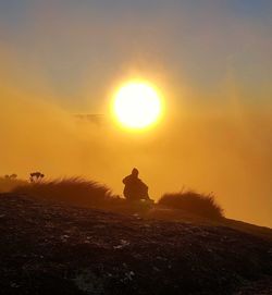 Silhouette person sitting on field against sky during sunset