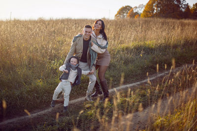 Stylish family with a boy child on a field in the dry grass in autumn