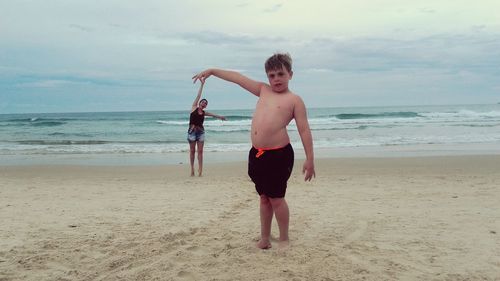 Full length of shirtless boy standing on beach against sky