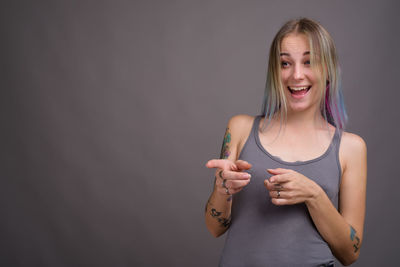 Portrait of smiling young woman standing against gray background