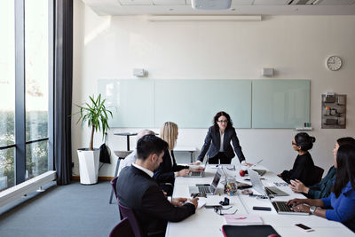 Businesswoman interacting with colleagues sitting at conference table during meeting in board room