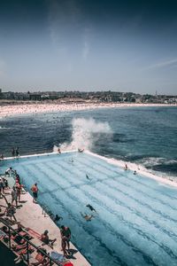 High angle view of people in swimming pool by sea against sky during sunny day