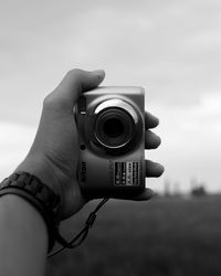 Close-up of hand holding camera against sky