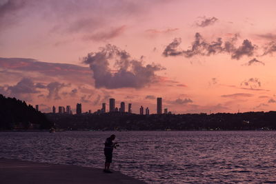 Man fishing by the sea against the sky during sunset