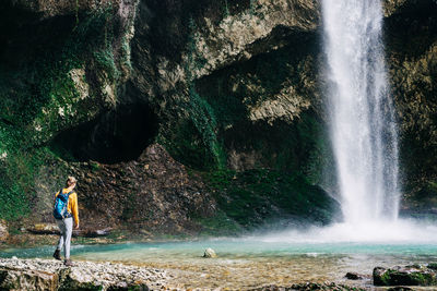 A woman hiker with a backpack in nature walks in a canyon near a waterfall and a stream