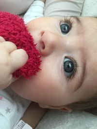 Close-up of cute baby girl with maroon stuffed toy on bed at home