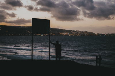 Silhouette man standing on beach against sky during sunset