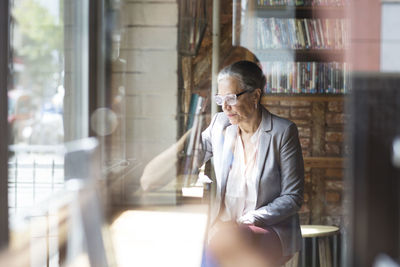 Serious mature woman sitting at table seen through glass in cafe