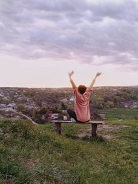 Woman sitting on bench in town against sky during sunset