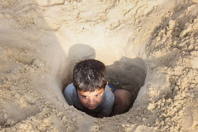 High angle view of boy sitting in sand hole at beach